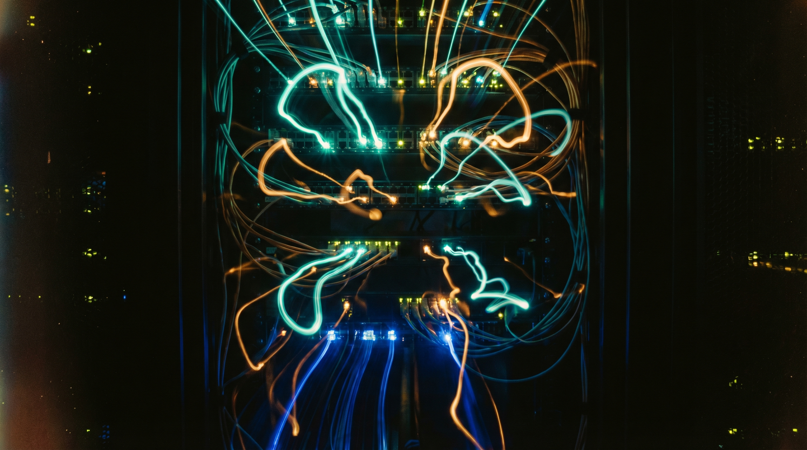 Long-exposure photography of fiber optic cables and network LEDs creating teal and amber light trails in a server room